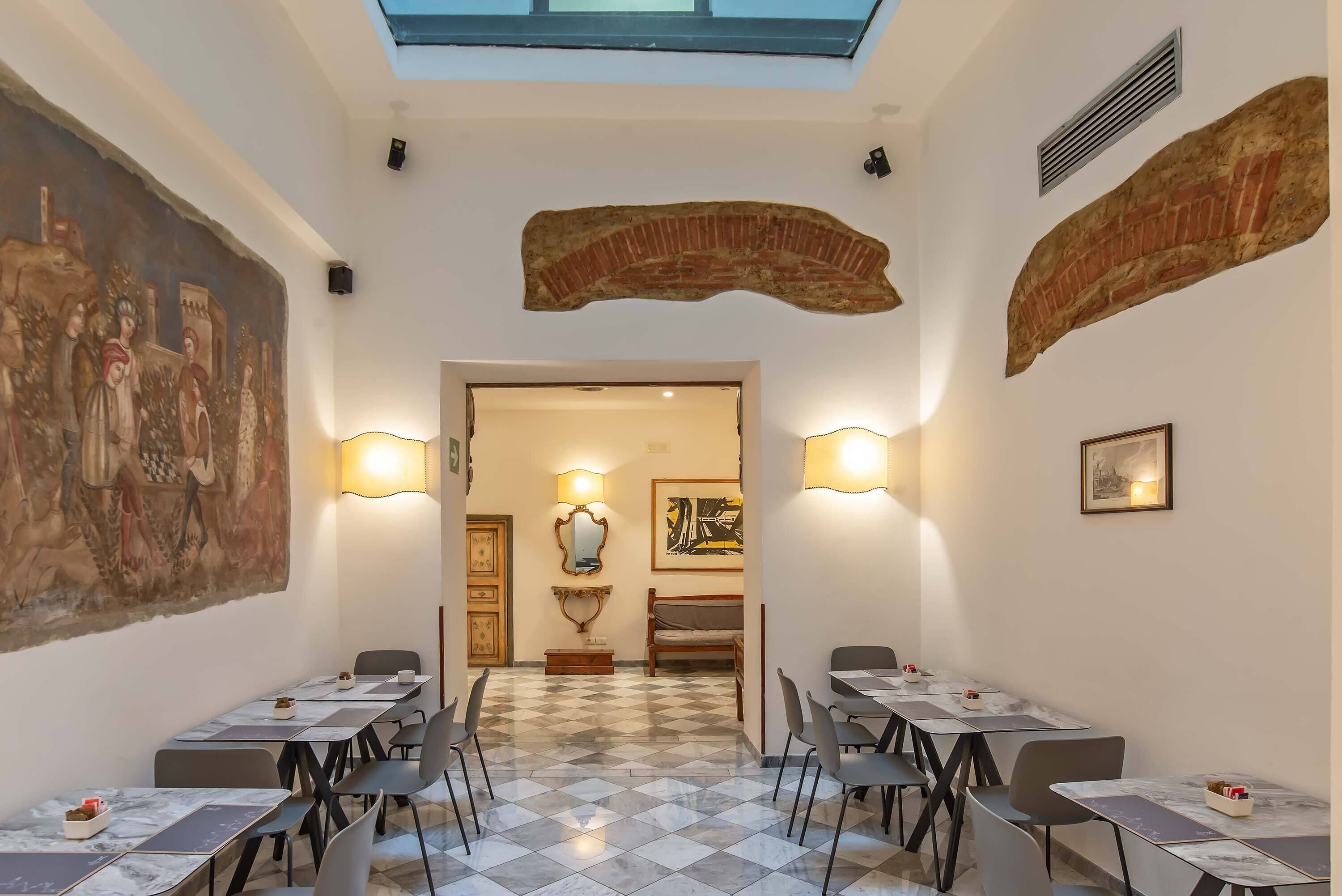 Un comedor con piso a cuadros, mesas con sillas y un mural grande en la pared.