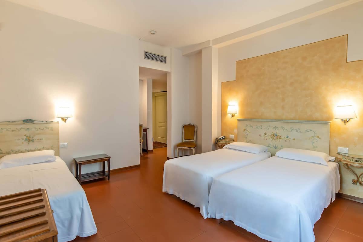A hotel room with two beds, a small table, a chair, and a lamp.