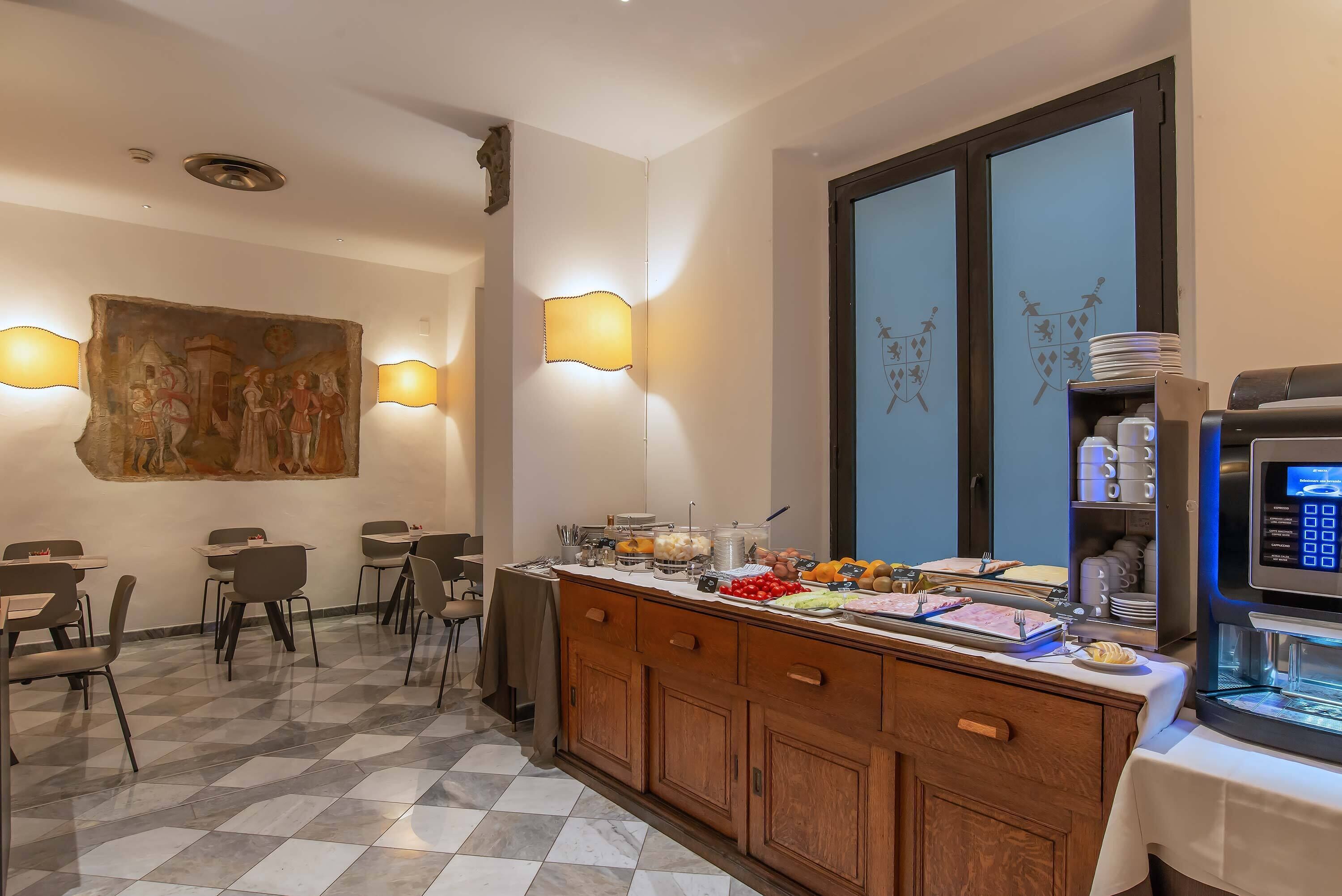 A hotel dining area with a checkered floor, wooden cabinets, a buffet counter, wall-mounted artwork, and wall sconces.