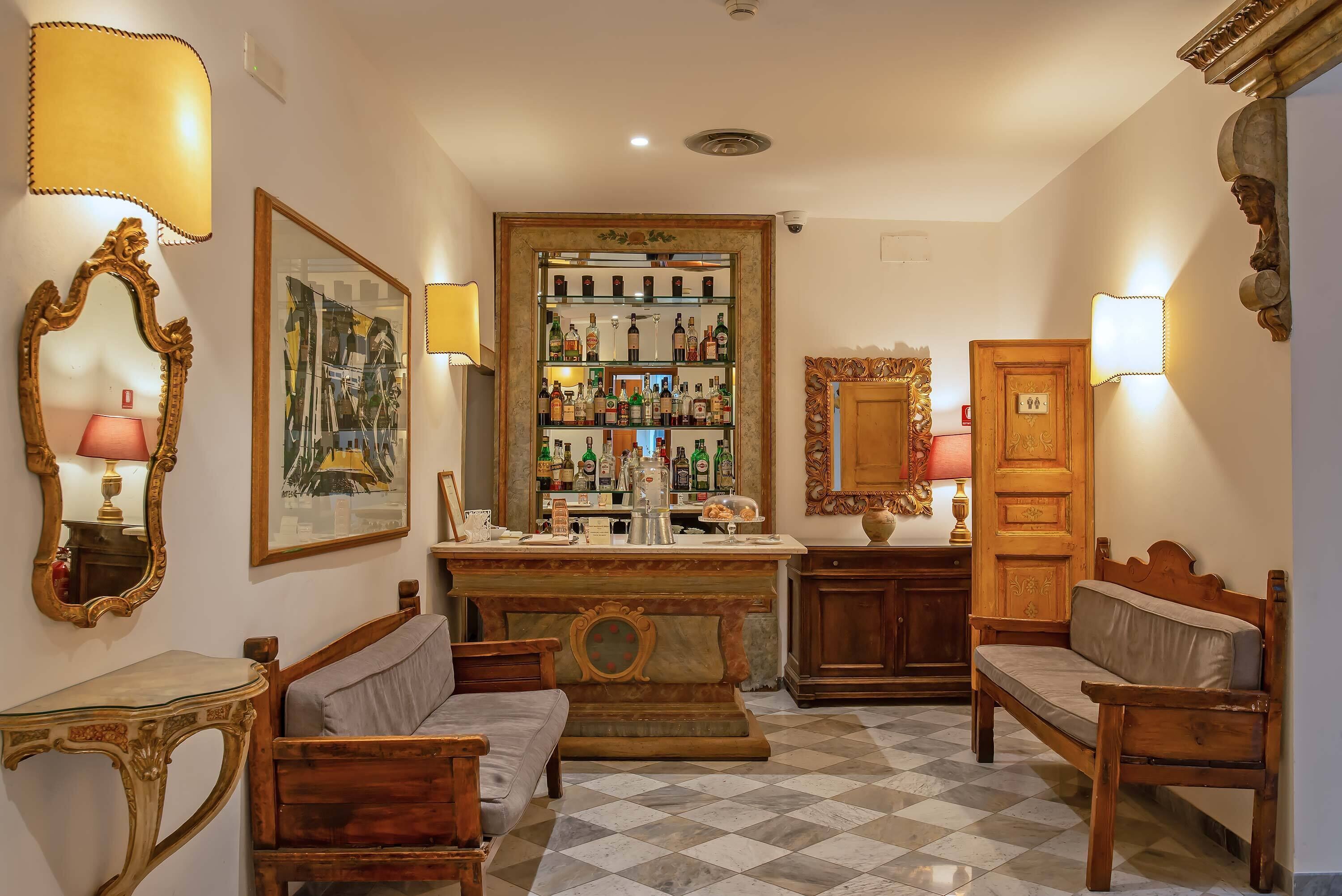 A bar area with shelves of bottles, a wooden counter, and two wooden chairs.