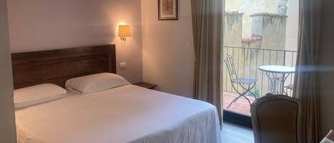 A hotel room with a bed, a bedside lamp, a framed picture on the wall, and a balcony with a table and chairs.