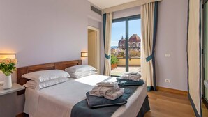 Habitación de hotel con cama, mesita de noche con un florero y vista a una estructura en forma de cúpula a través de la ventana.