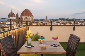 A table with drinks and snacks on a balcony overlooking a cityscape with domed buildings. - Hotel Machiavelli Palace (Florence)