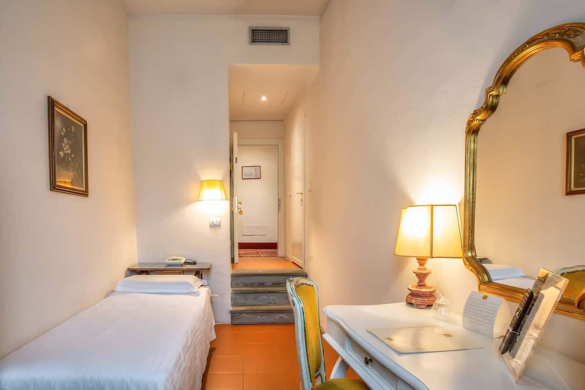 A hotel room with two single beds, a desk with a lamp, a mirror, and a staircase leading to another room.