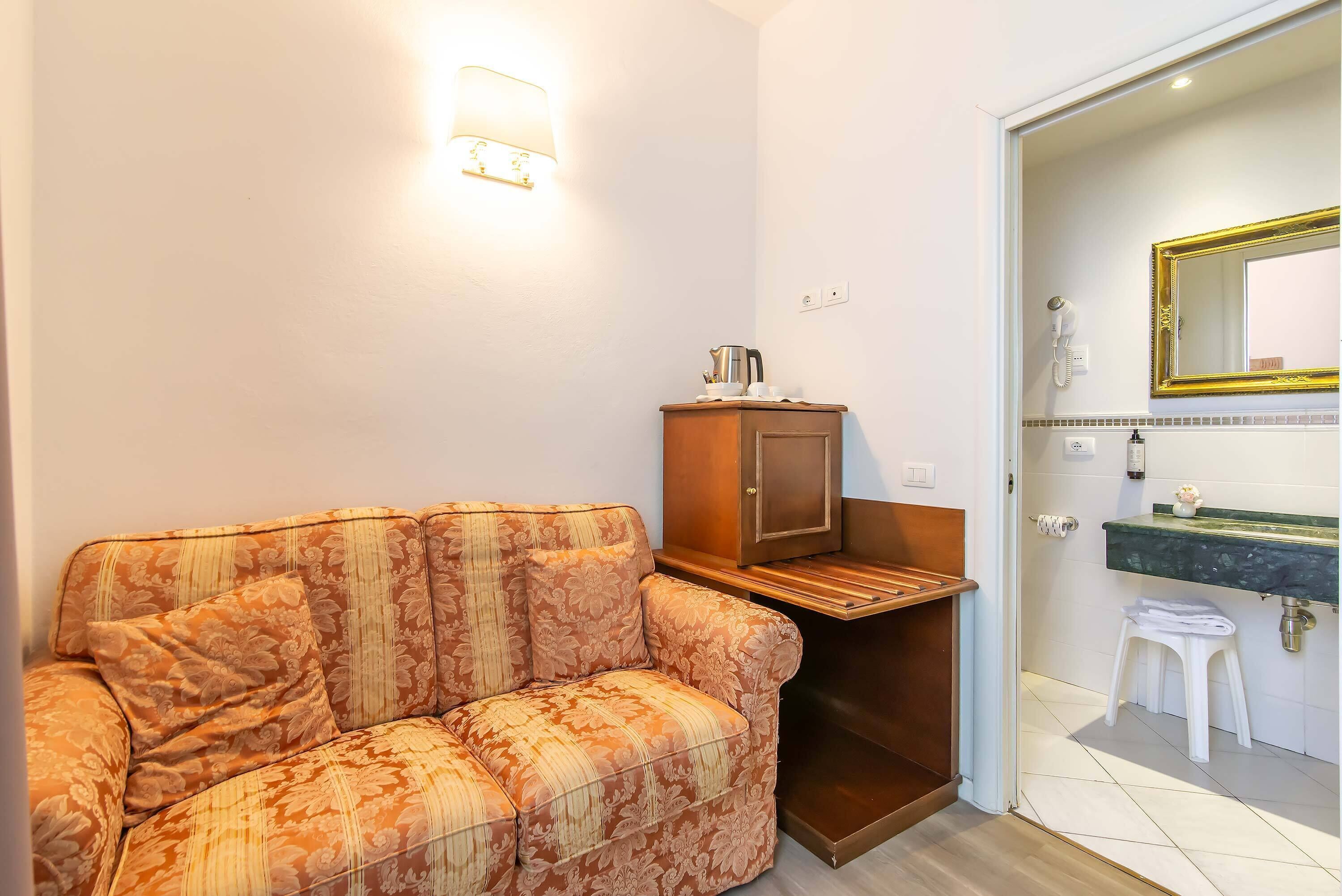 A room with a sofa, a cabinet, a small stool, a sink, and a mirror.