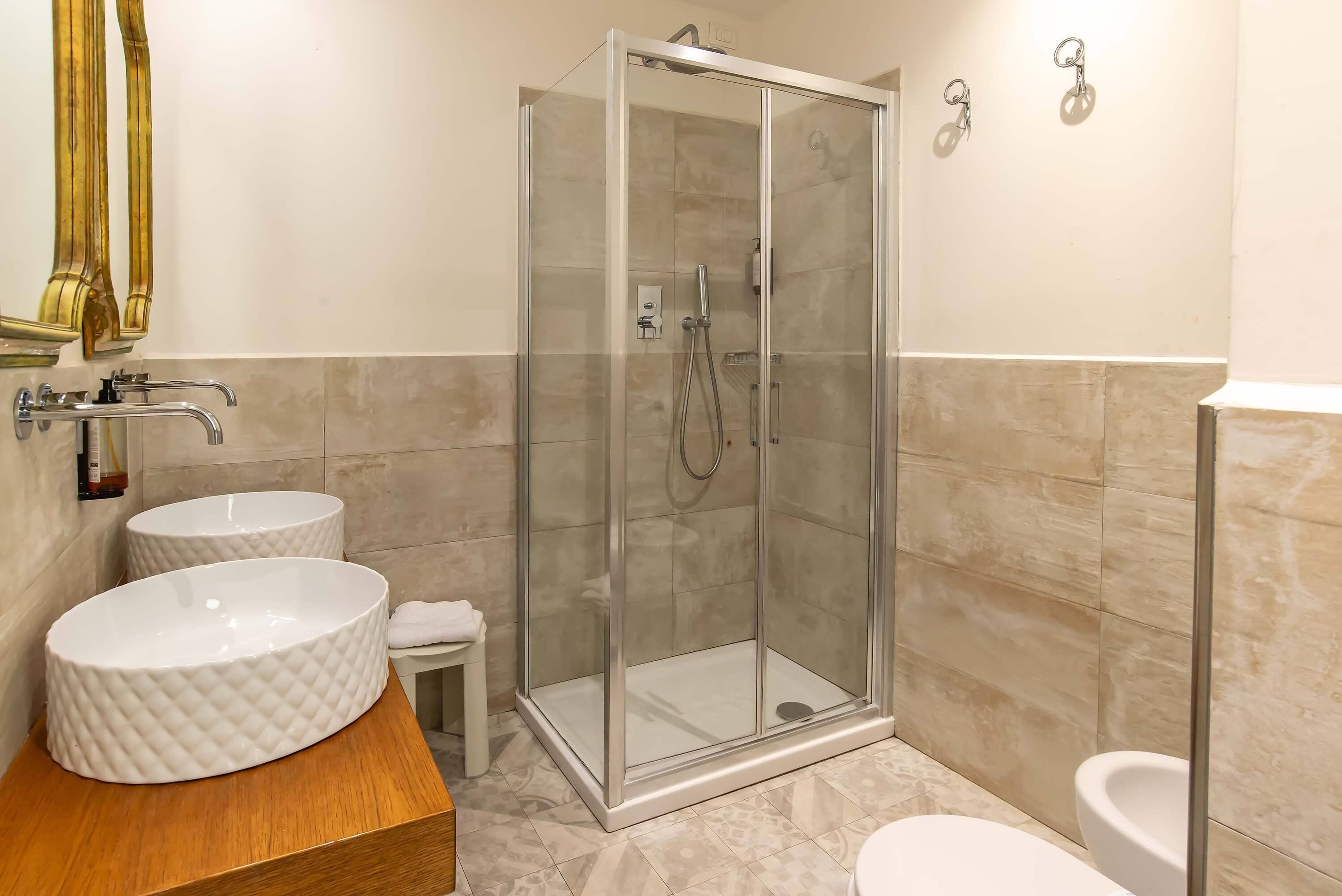 Une salle de bain moderne avec une douche à parois de verre, deux lavabos ronds et des toilettes.