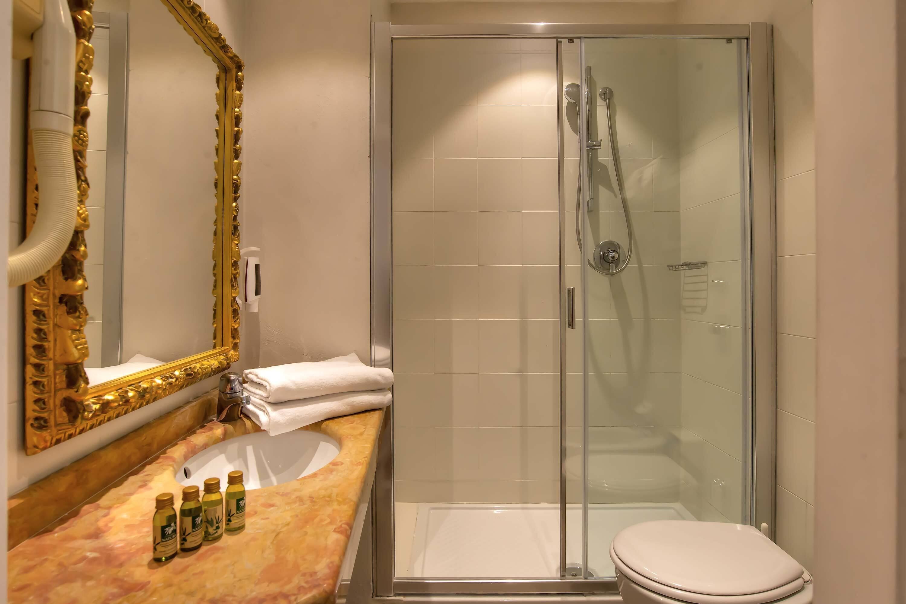 A bathroom with a glass-enclosed shower, a marble sink, and a toilet.