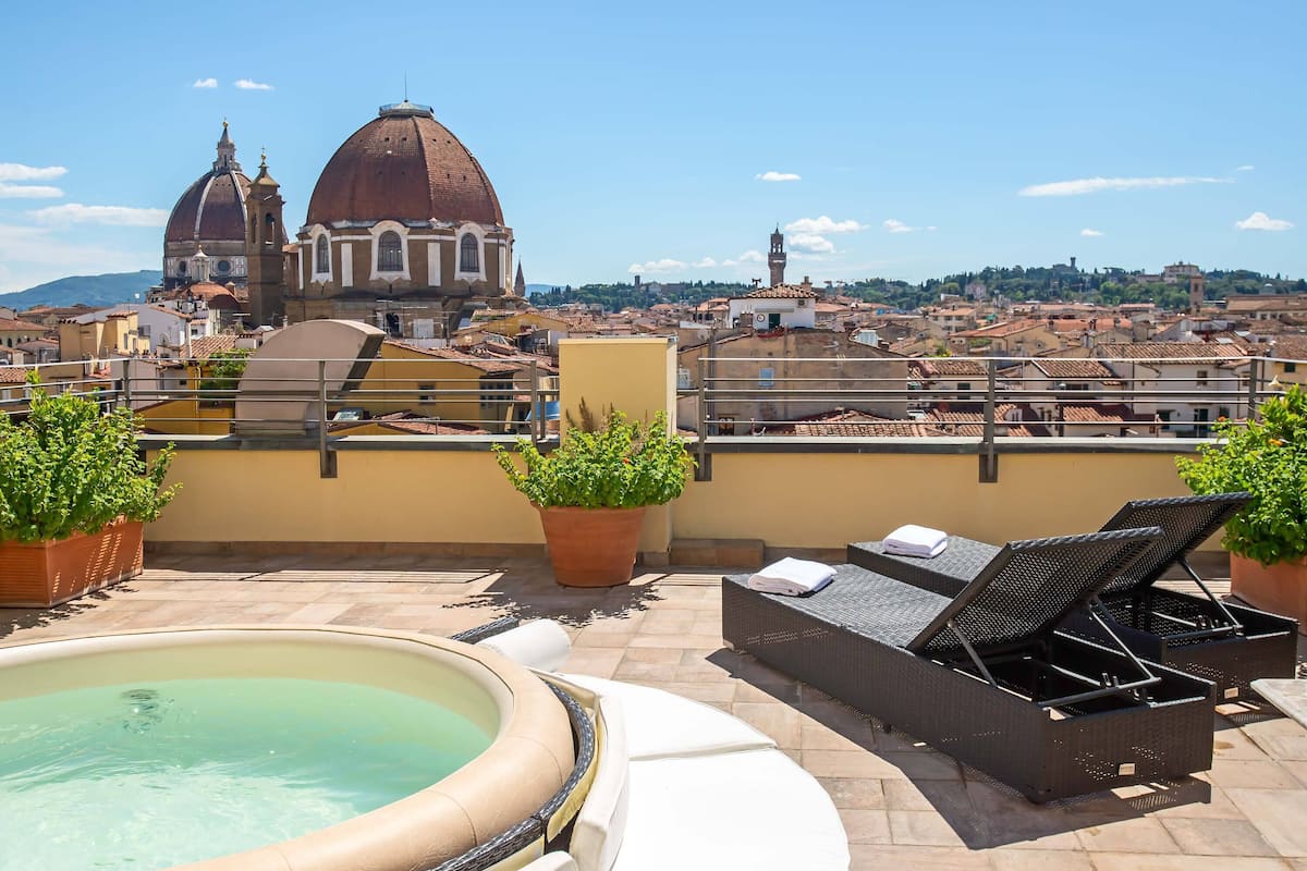 A rooftop terrace with a hot tub, lounge chairs, and potted plants.