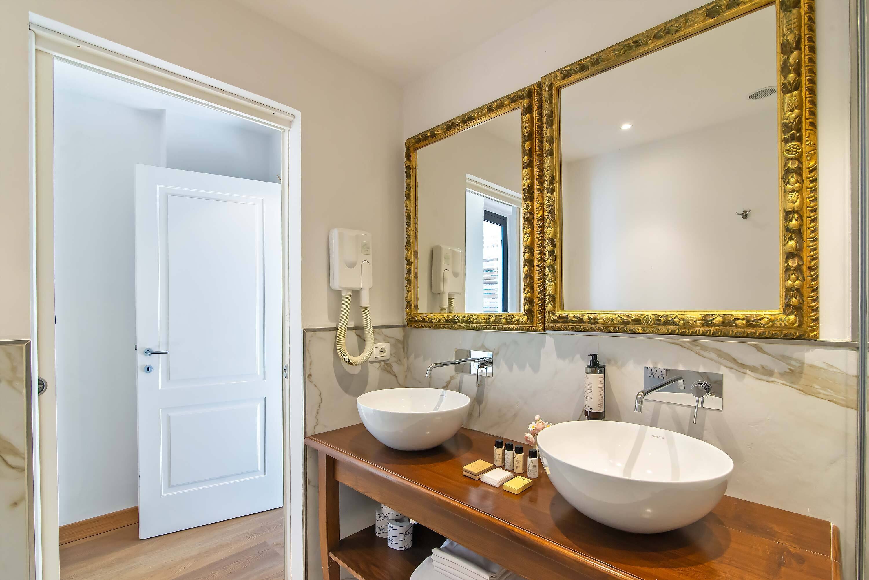 A bathroom with a white door, two sinks, a large mirror with a gold frame, and a marble wall.