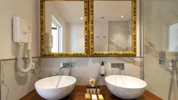 A bathroom with two large white sinks, a gold-framed mirror, a handheld showerhead, and a hand soap dispenser.