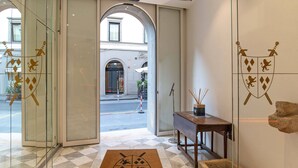 Entrada de hotel con puerta de vidrio, felpudo con escudo, consola de madera y escultura de piedra.