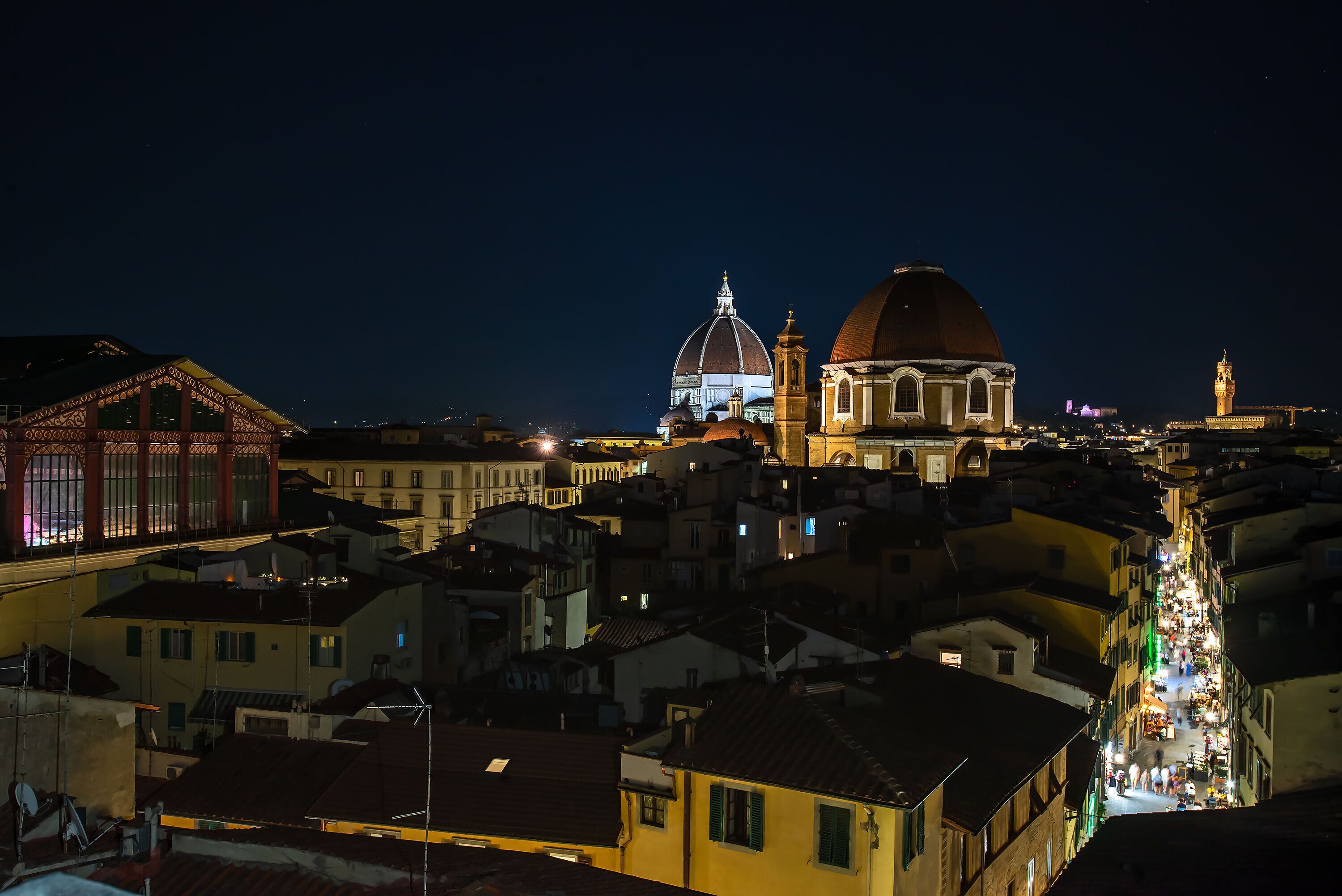 A nighttime view of a densely packed urban area with historic buildings, including a prominent dome and bell tower.