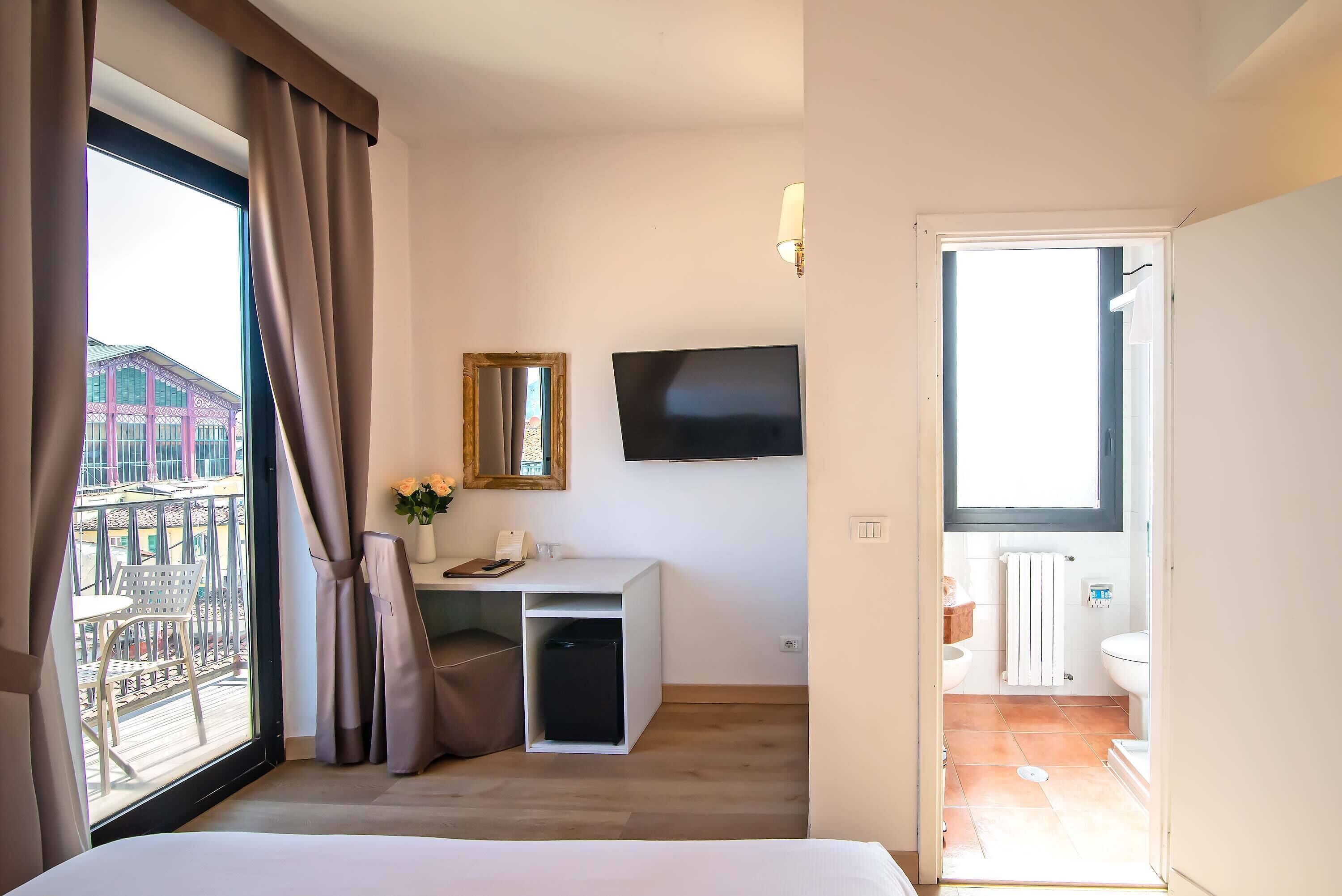 Ein Hotelzimmer mit Bett, Schreibtisch, Fernseher, Balkon mit Sitzgelegenheit und Bad.
