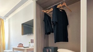 A modern room with a wooden wardrobe, a flat-screen TV, a desk with a chair, and a small plant. - Hotel Gioia (Florence)