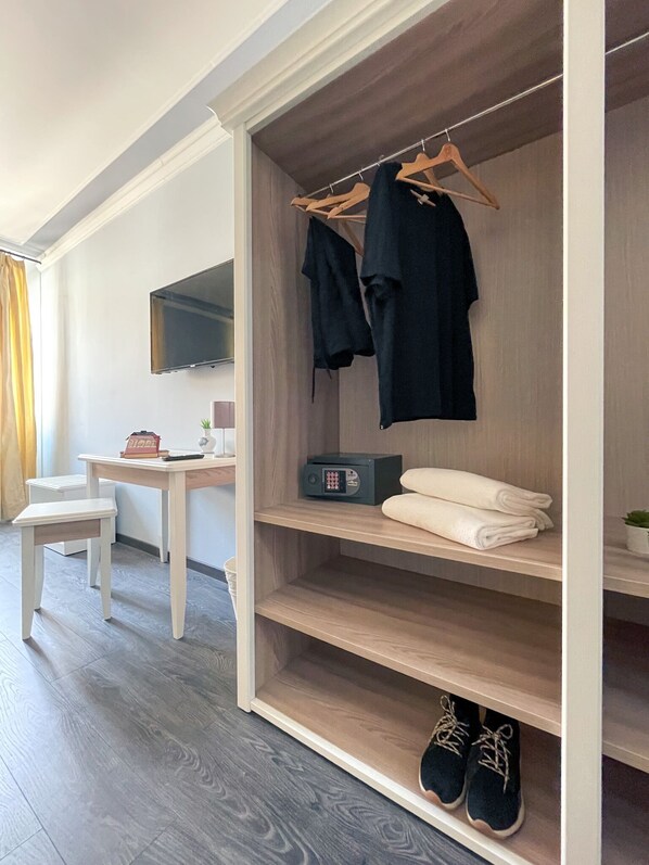 A modern room with a wooden wardrobe, a flat-screen TV, a desk with a chair, and a small plant.