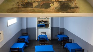 A dining area with tables covered in blue tablecloths and a mural of a historic bridge above. - Hotel Gioia (Florence)
