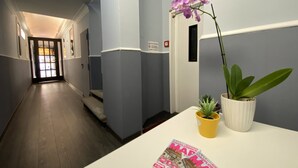 A hallway with a white reception desk, a potted plant, and a magazine on the desk. - Hotel Gioia (Florence)
