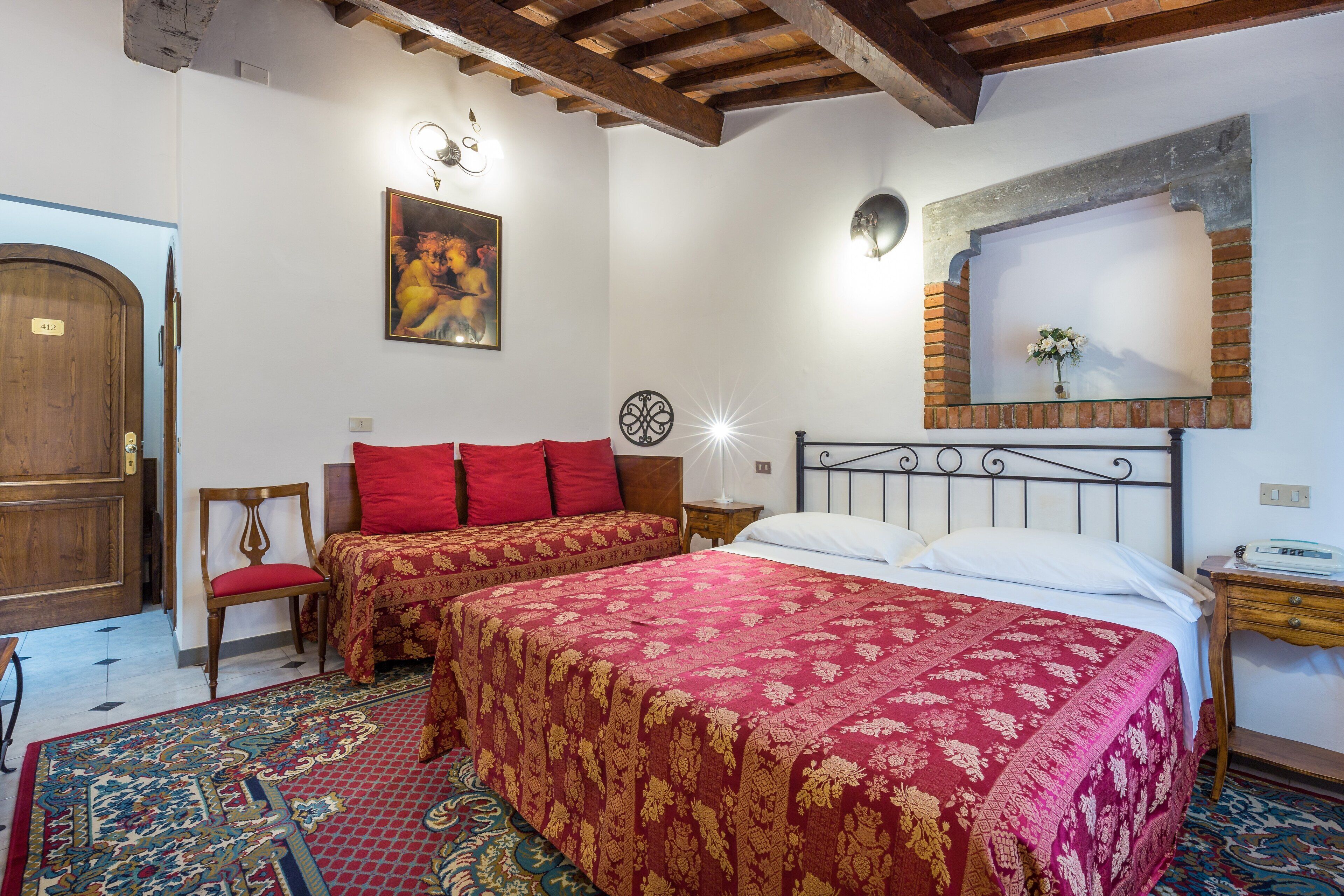 A room with two beds, a wooden door, a chair, a nightstand, and a painting on the wall.