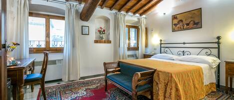 A bedroom with a wooden ceiling, a bed with a patterned bedspread, a chair, a desk, and a window with curtains.