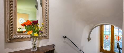 A staircase with a wooden handrail, a mirror with a decorative frame, and a vase with flowers on a wooden console table.