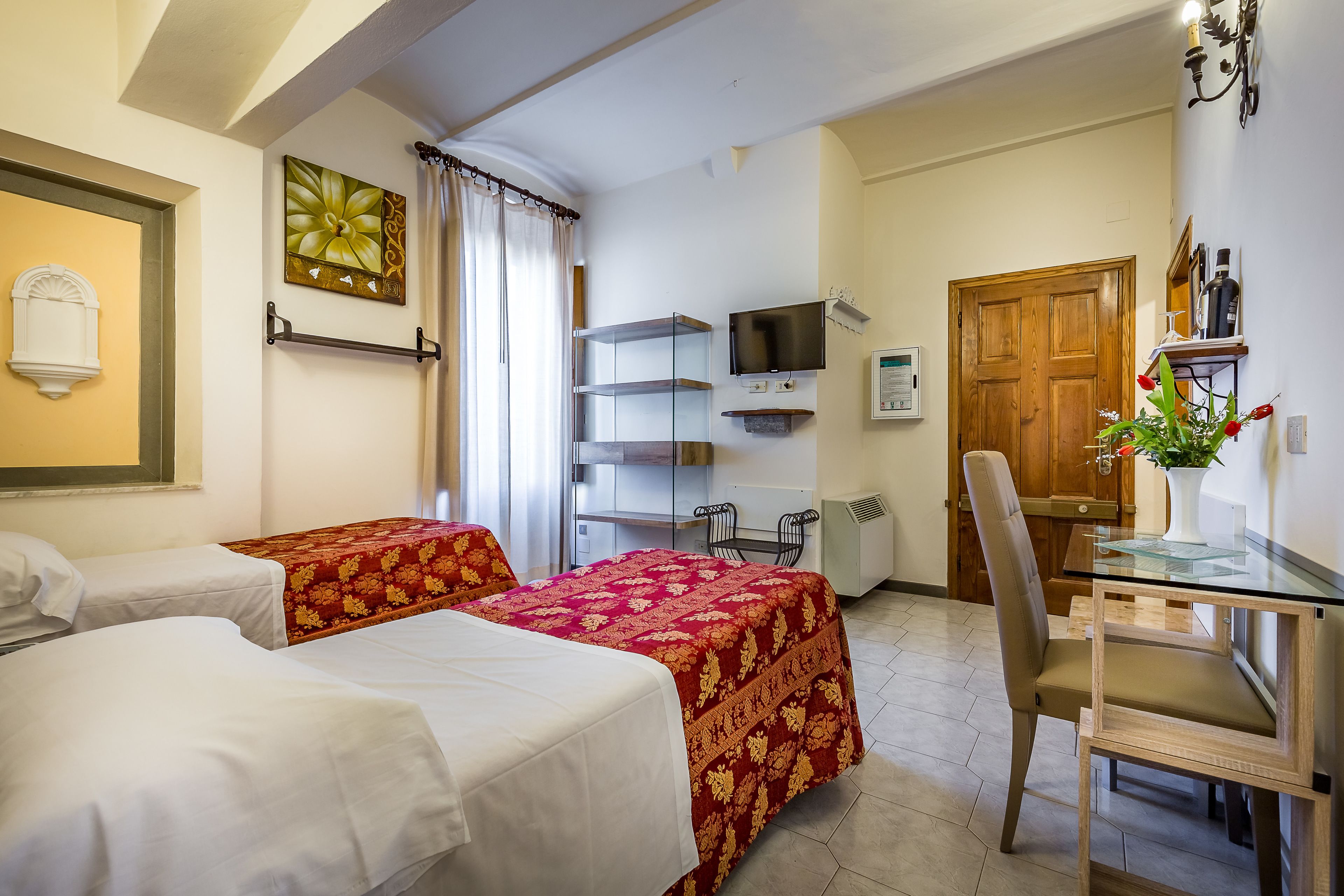 A hotel room with two beds, a desk with a chair, a TV, and a wooden door.