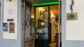 La entrada del Hotel Collodi, con un cartel sobre la puerta, una reja de hierro forjado y el interior iluminado en verde visible a través del escaparate.