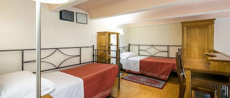 A room with two single beds, a wooden desk, a chair, a lamp, and a small cabinet.