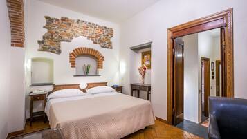 Habitación de hotel con cama, mesita de noche, espejo, silla de madera y pared de piedra.