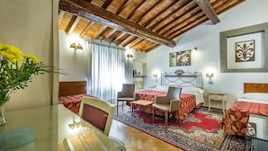 Habitación de hotel con techo de madera, cama con ropa de cama roja, una pequeña mesa con sillas y una alfombra decorativa.