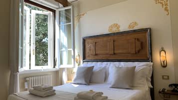 Ein ordentlich bezogenes Bett mit weißen Leinen und Handtüchern, ein Holz-Kopfteil, ein Heizkörper und ein Fenster mit Vorhängen.