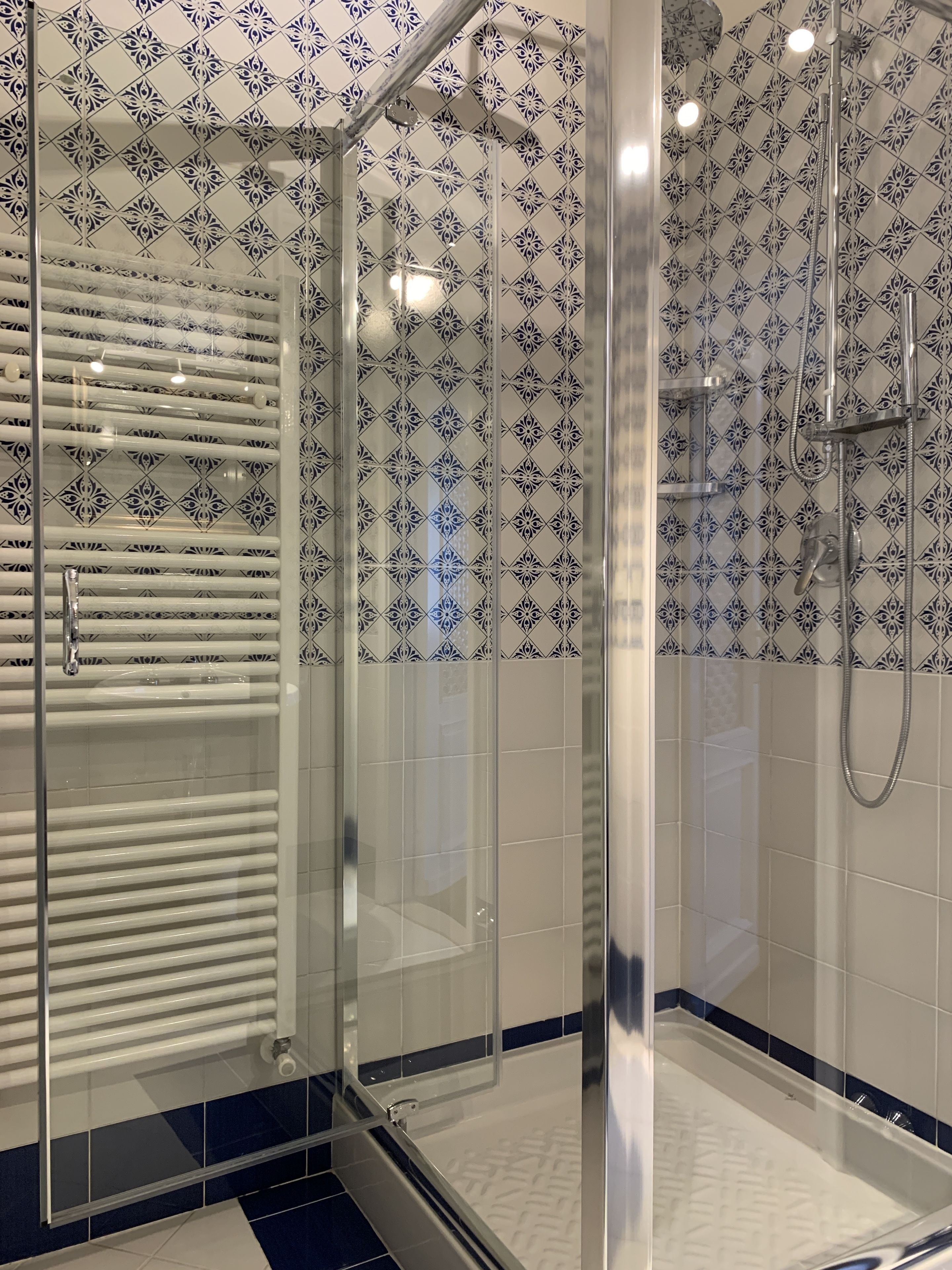 Un baño moderno con ducha envuelta en vidrio, azulejos blancos y un salpicadero decorado.