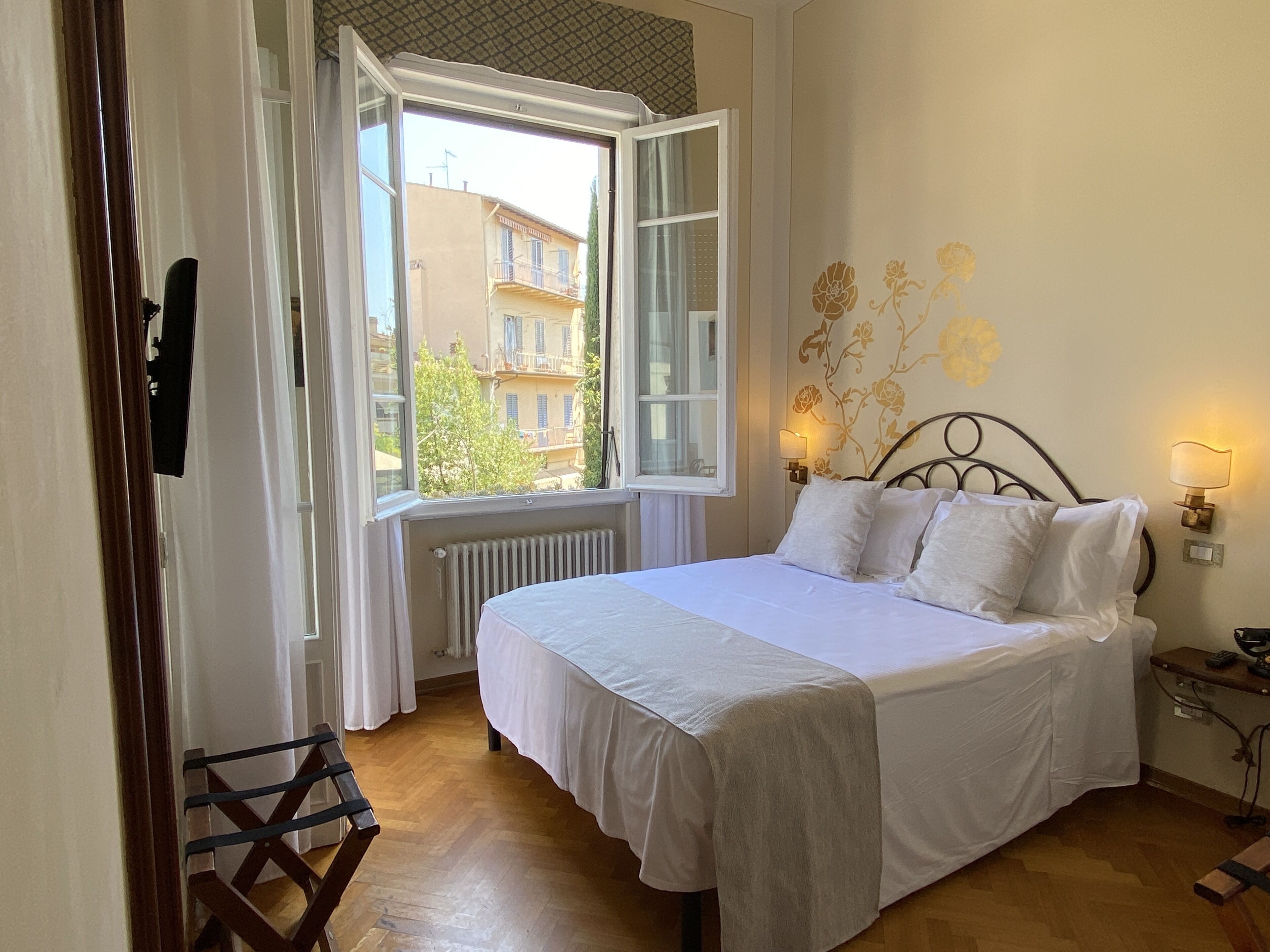 A bedroom with a bed, a window, a radiator, and a wall-mounted lamp.
