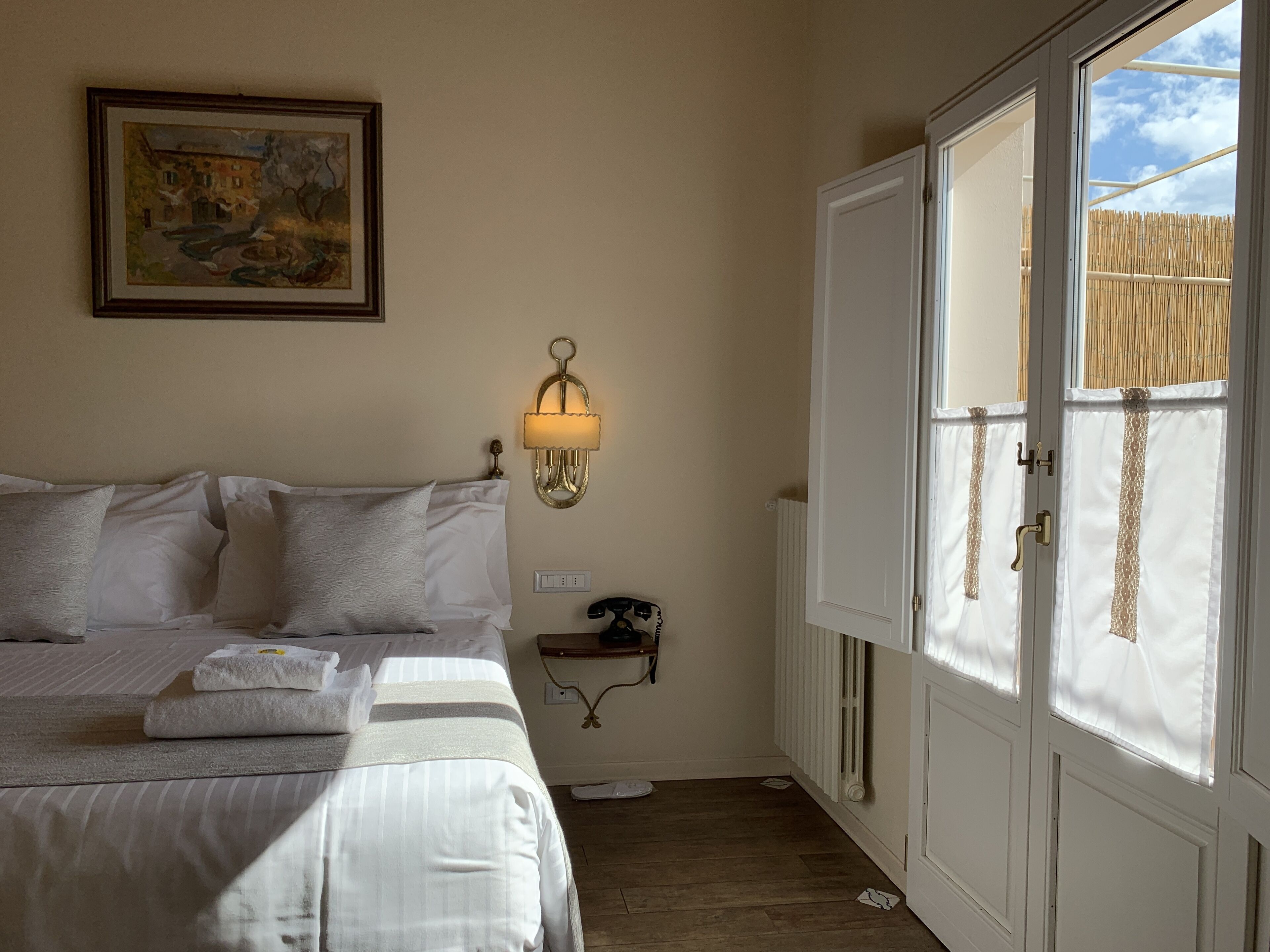 Un dormitorio con cama, una lámpara de pared, un radiador y una ventana con vistas a una valla de bambú.