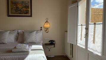 Un dormitorio con cama, una lámpara de pared, un radiador y una ventana con vistas a una valla de bambú.