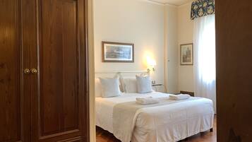 Habitación de hotel con armario de madera, cama con ropa blanca, mesita de noche y lámpara de pared.