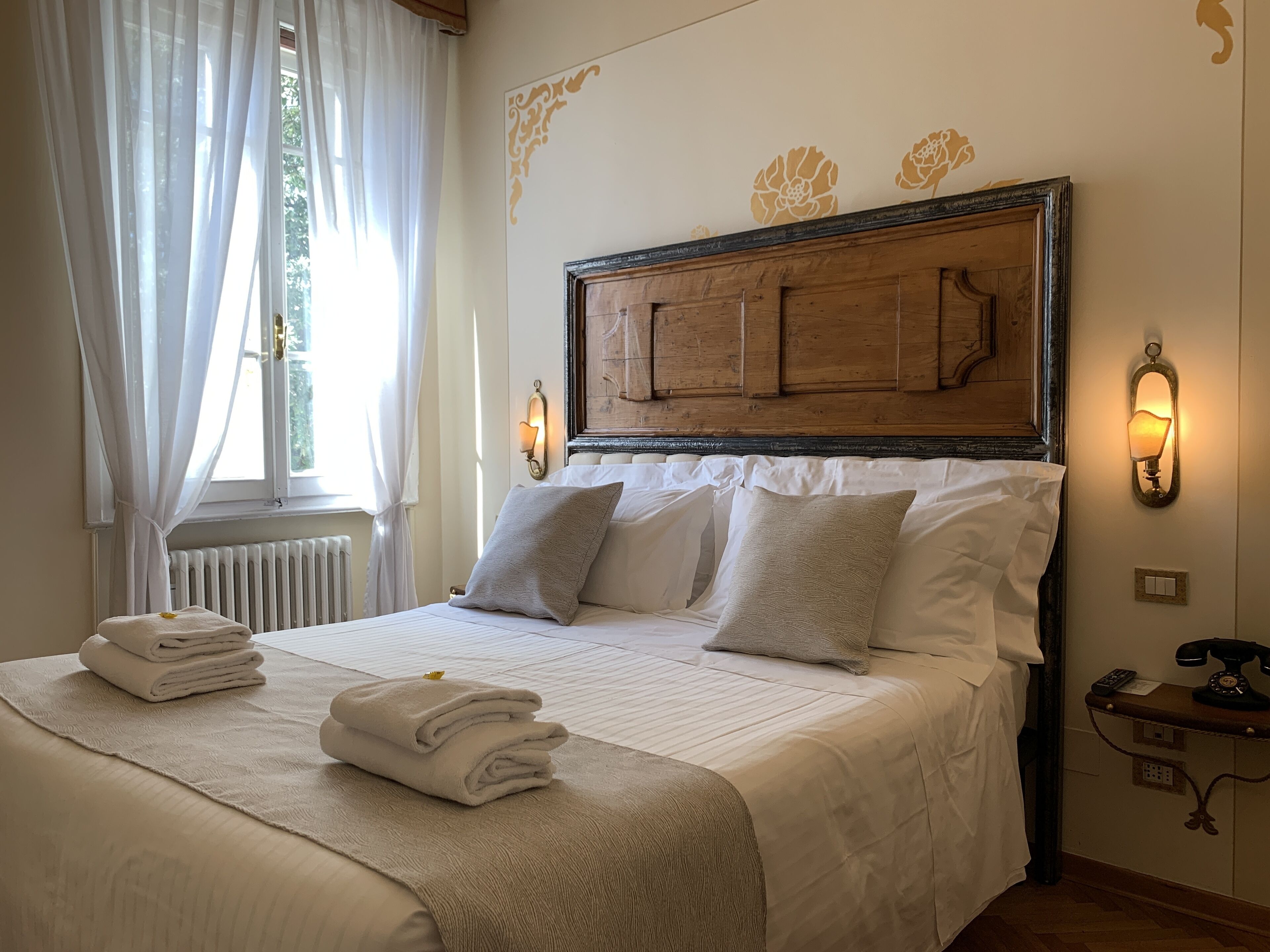 Een net opgemaakt bed met een houten hoofdbord, witte lakens en een nachtkastje met een lamp en telefoon.