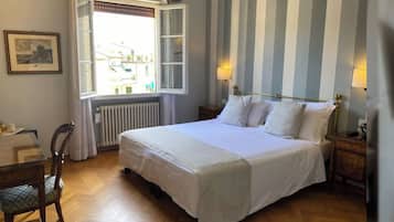 Una cama bien hecha en una habitación con paredes a rayas, una ventana con cortinas y un radiador.