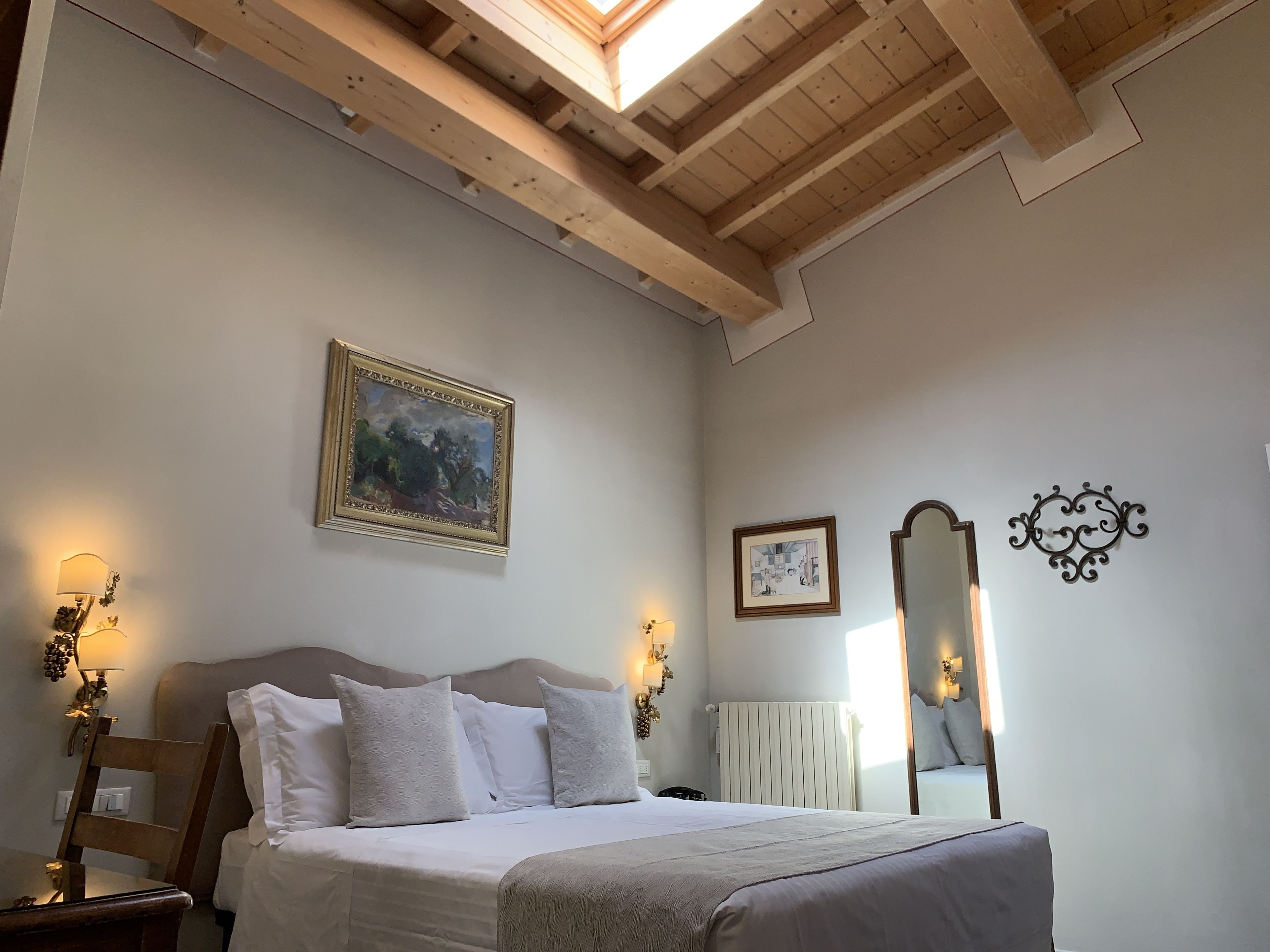 Un dormitorio con cama, techo de madera, un cuadro, espejo y apliques de pared.