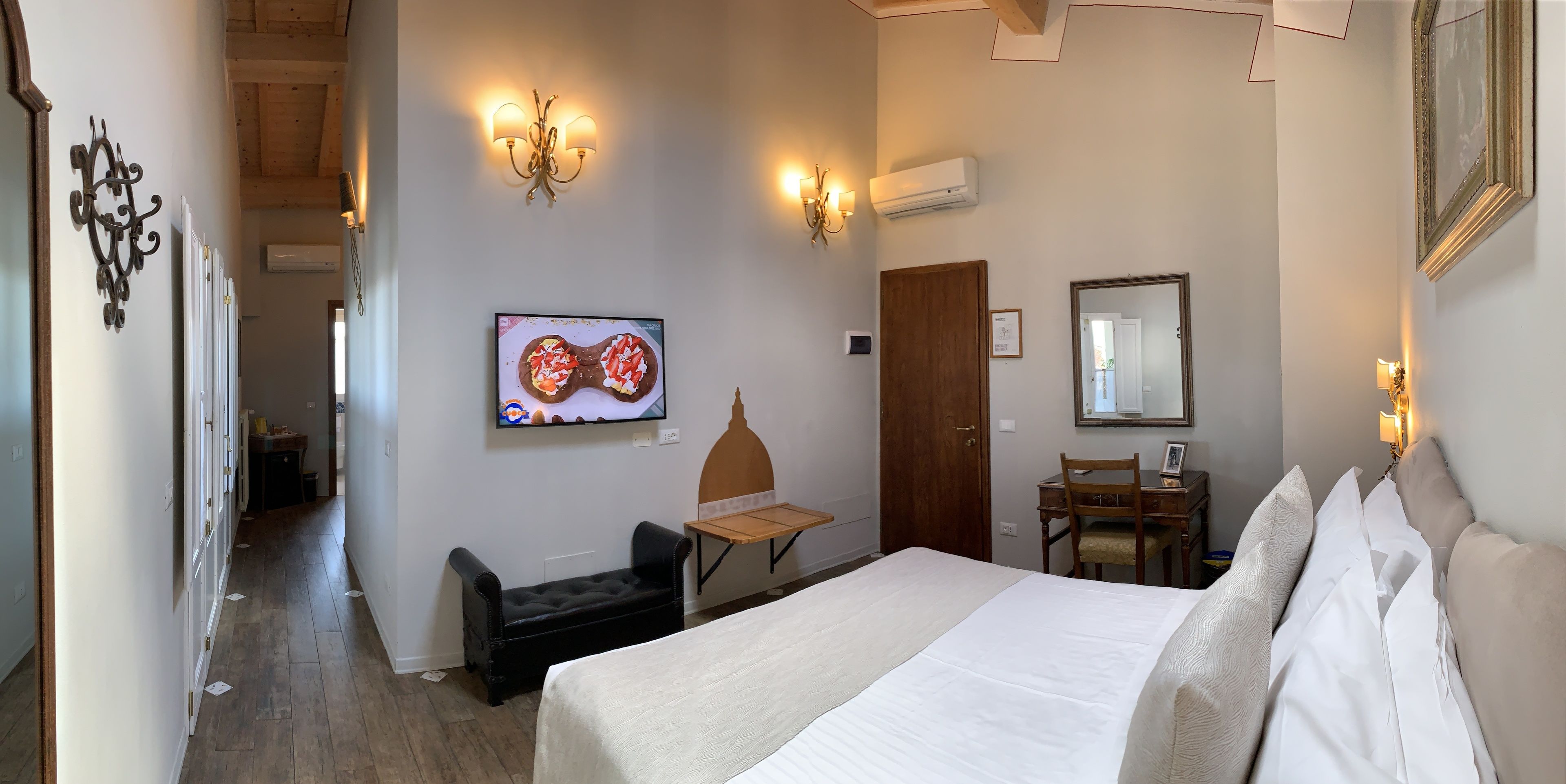 Una camera d'albergo con un letto, una scrivania, una sedia, una TV e un armadio.