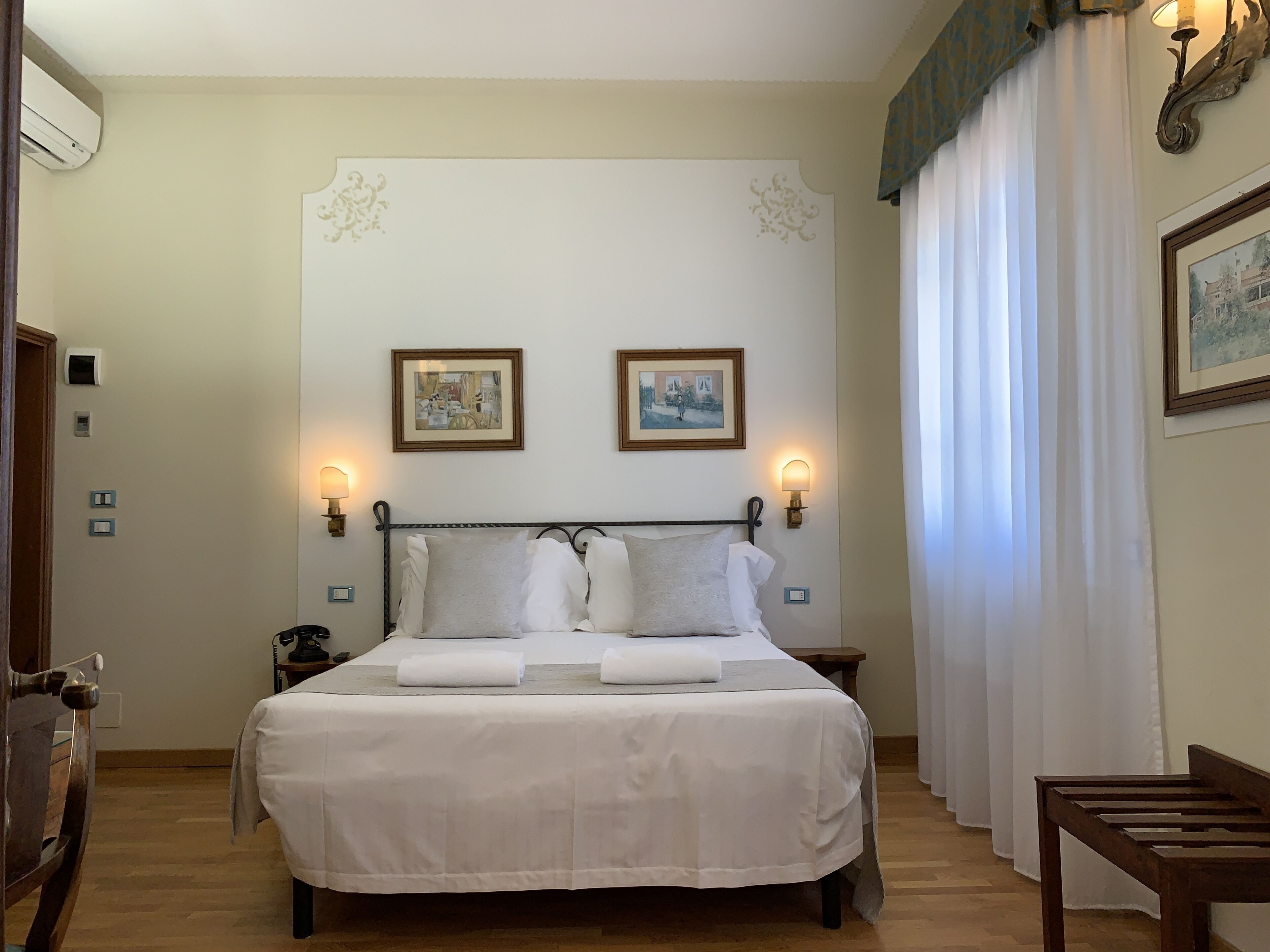 A neatly made bed with white linens and pillows, two wall-mounted lamps, and two framed pictures above the bed.