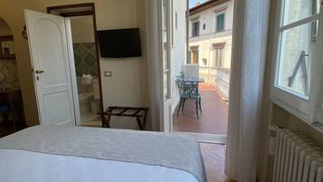 Une chambre à coucher avec un lit, une télévision et une vue sur une cour intérieure, où se trouvent une chaise et une table.