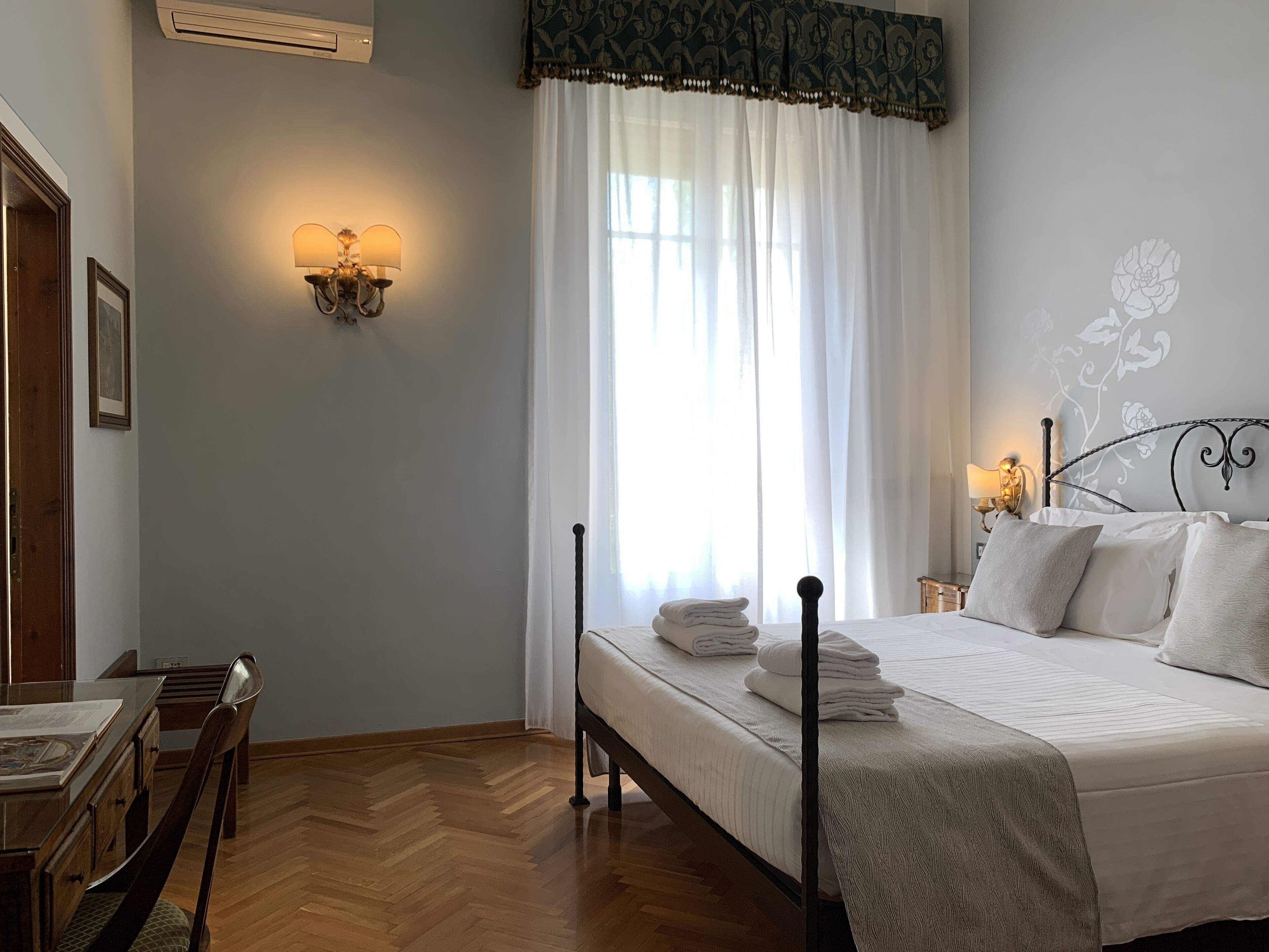 A bedroom with a bed, bedside lamps, a wooden desk, and a chair.