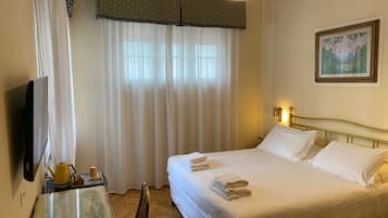 Una habitación de hotel con una cama, un televisor, una mesita de noche con lámpara y un cuadro en la pared.