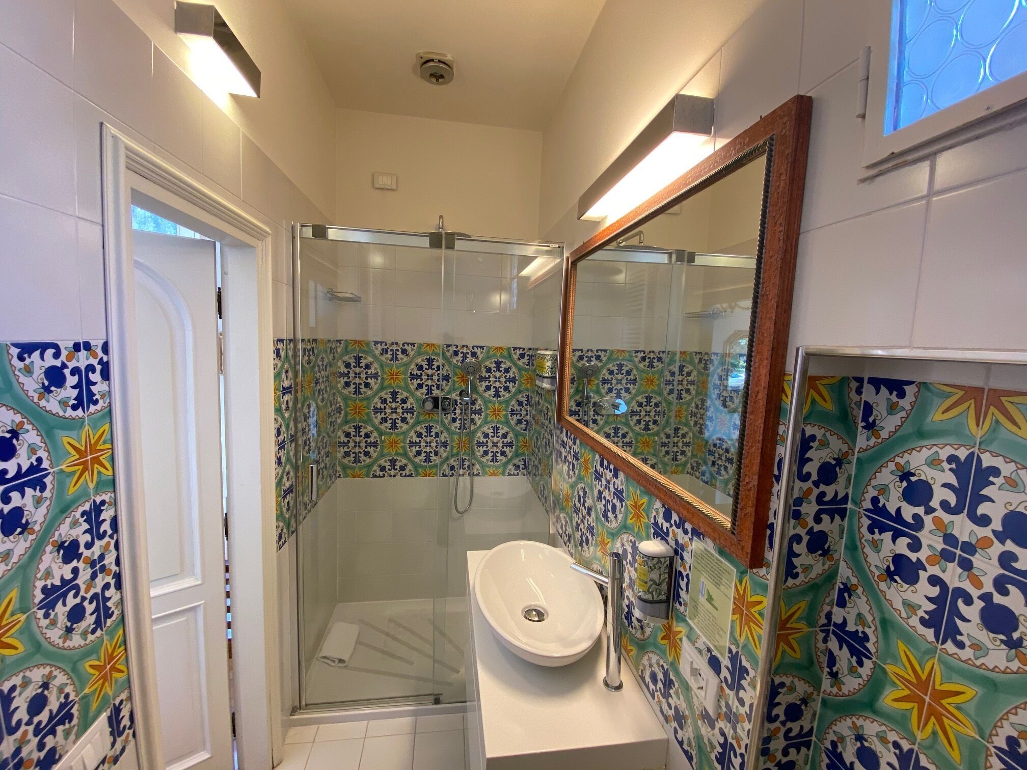 Un baño con cabina de ducha de vidrio, un lavamanos blanco y un espejo.
