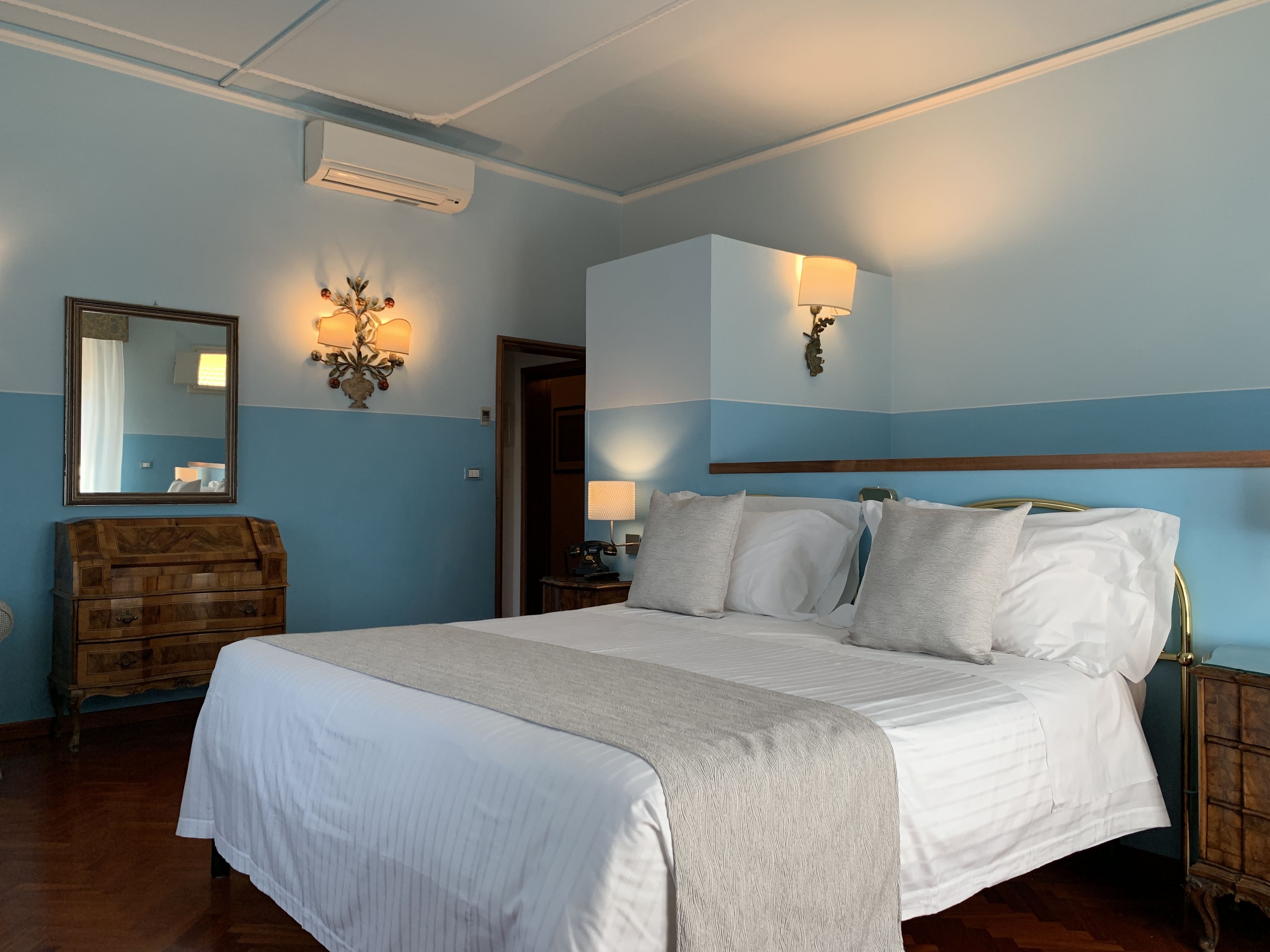 Un dormitorio con una cama grande, un aparador de madera, un espejo y lámparas de pared.