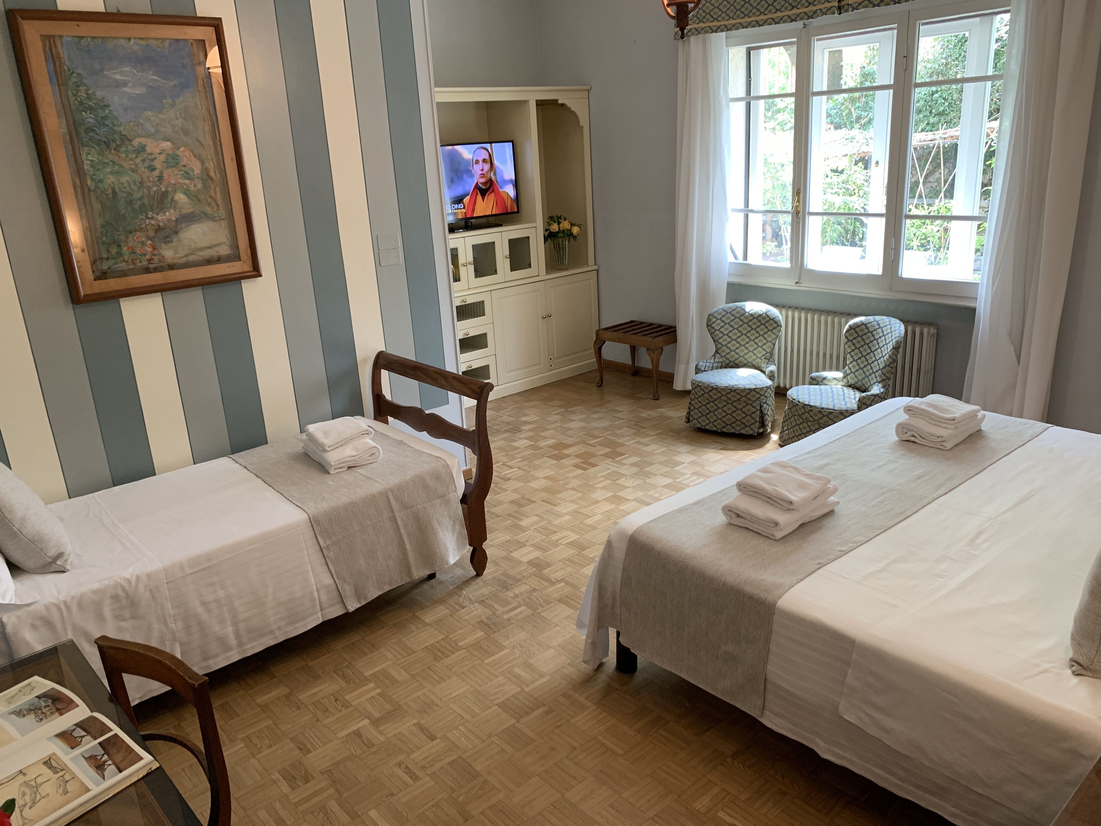 Une chambre d’hôtel avec deux lits simples, une télévision, un tableau et une fenêtre donnant sur un paysage verdoyant.