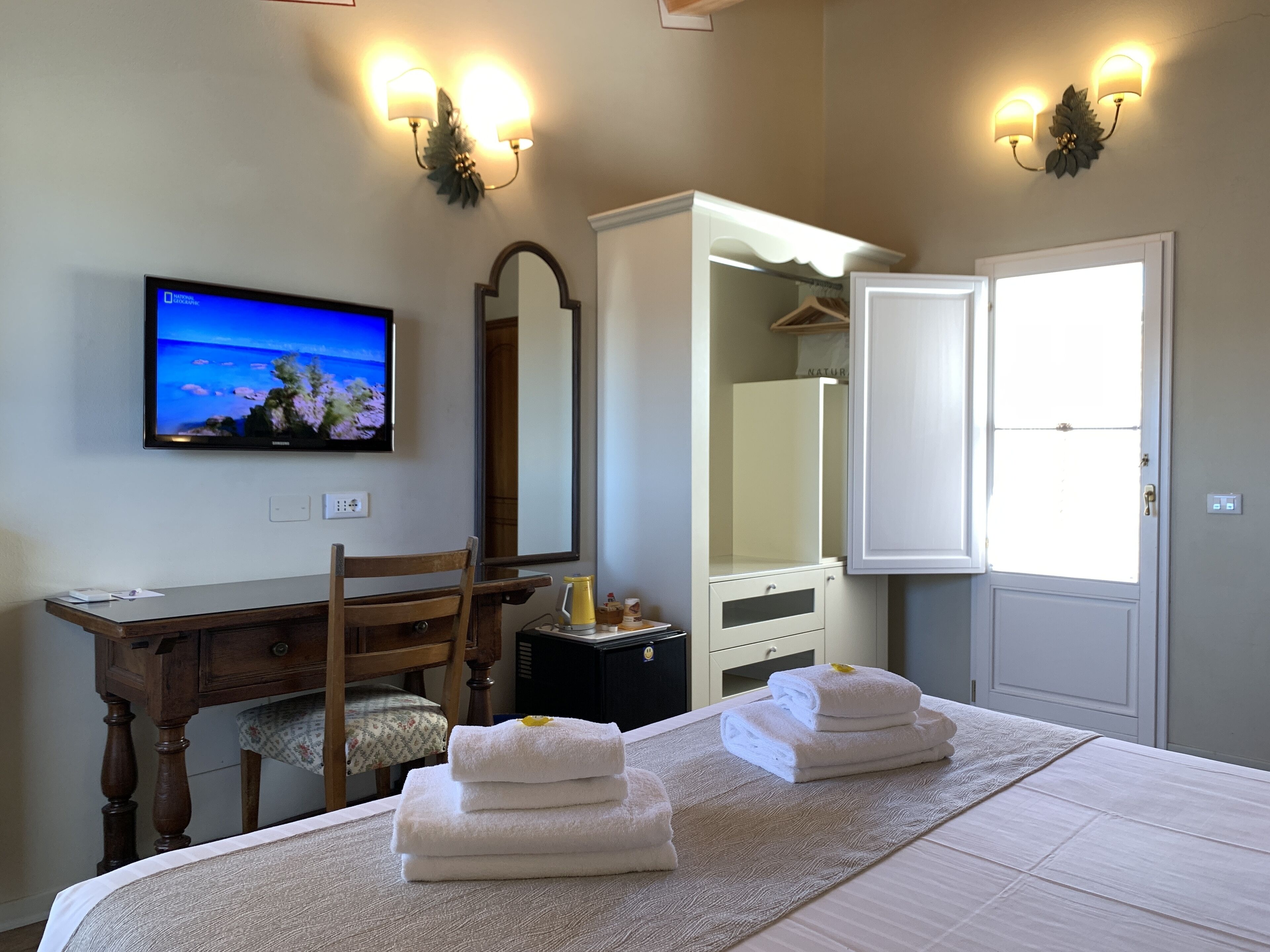 Habitación de hotel con cama, escritorio, silla, televisor, armario y puerta.