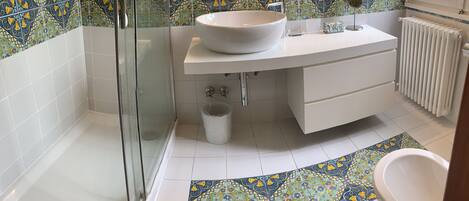A bathroom with a glass-enclosed shower, a white sink with a vessel basin, a white vanity, and a patterned floor.