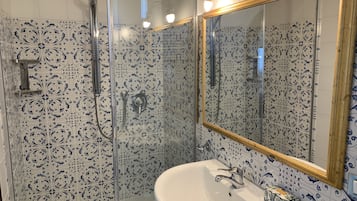 Un baño con un lavamanos blanco, un espejo y una ducha con puerta de cristal.
