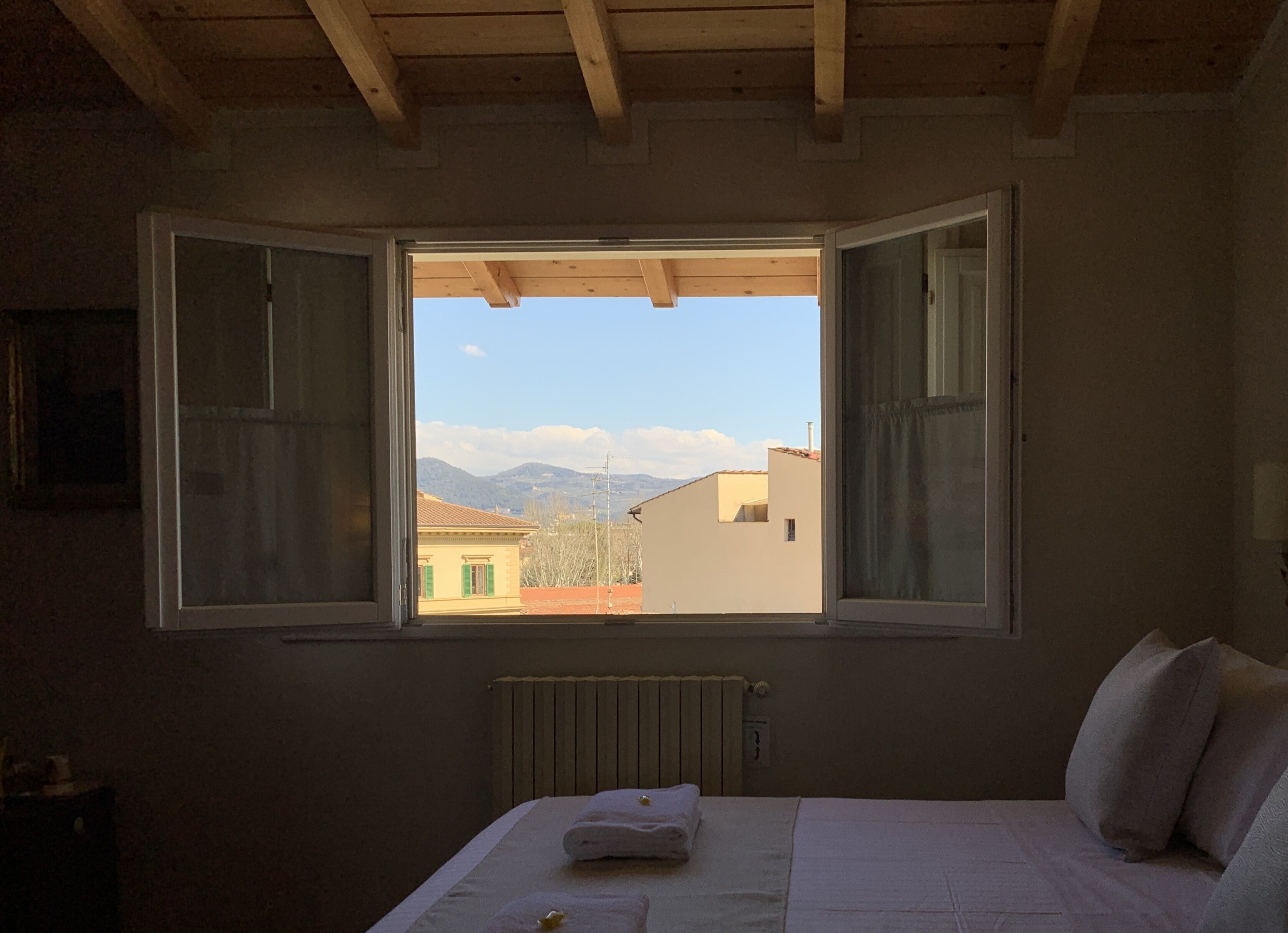 Une chambre avec une grande fenêtre, un lit recouvert d’une couette blanche et un radiateur.